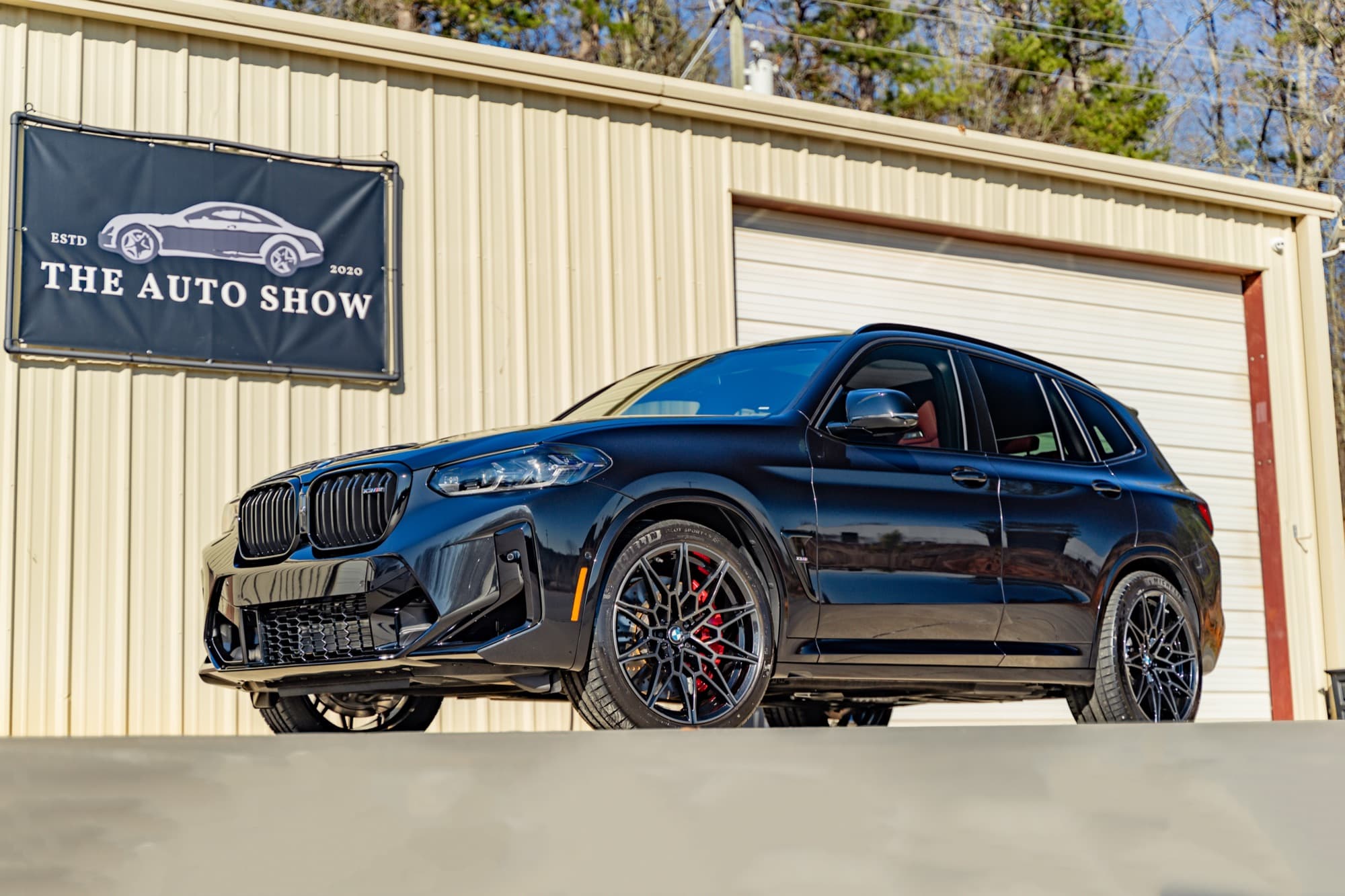 A black BMW SUV with red brake calipers parked in front of The Auto Show building
