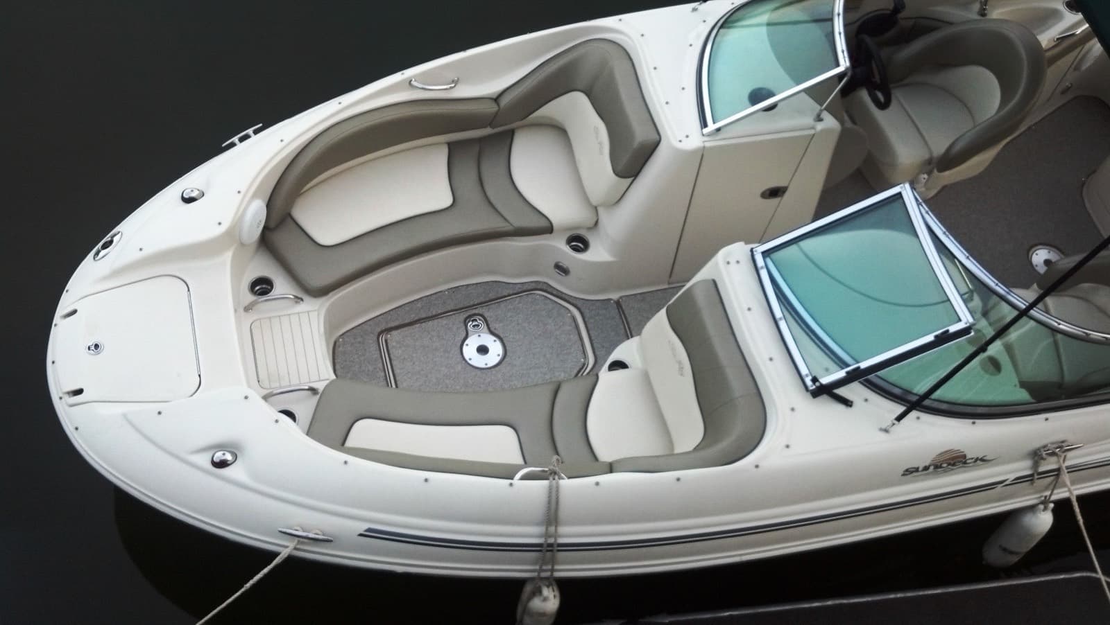 Overhead view of a white bowrider's open bow showing gray and white vinyl seats, a textured non-skid floor and a split windshield