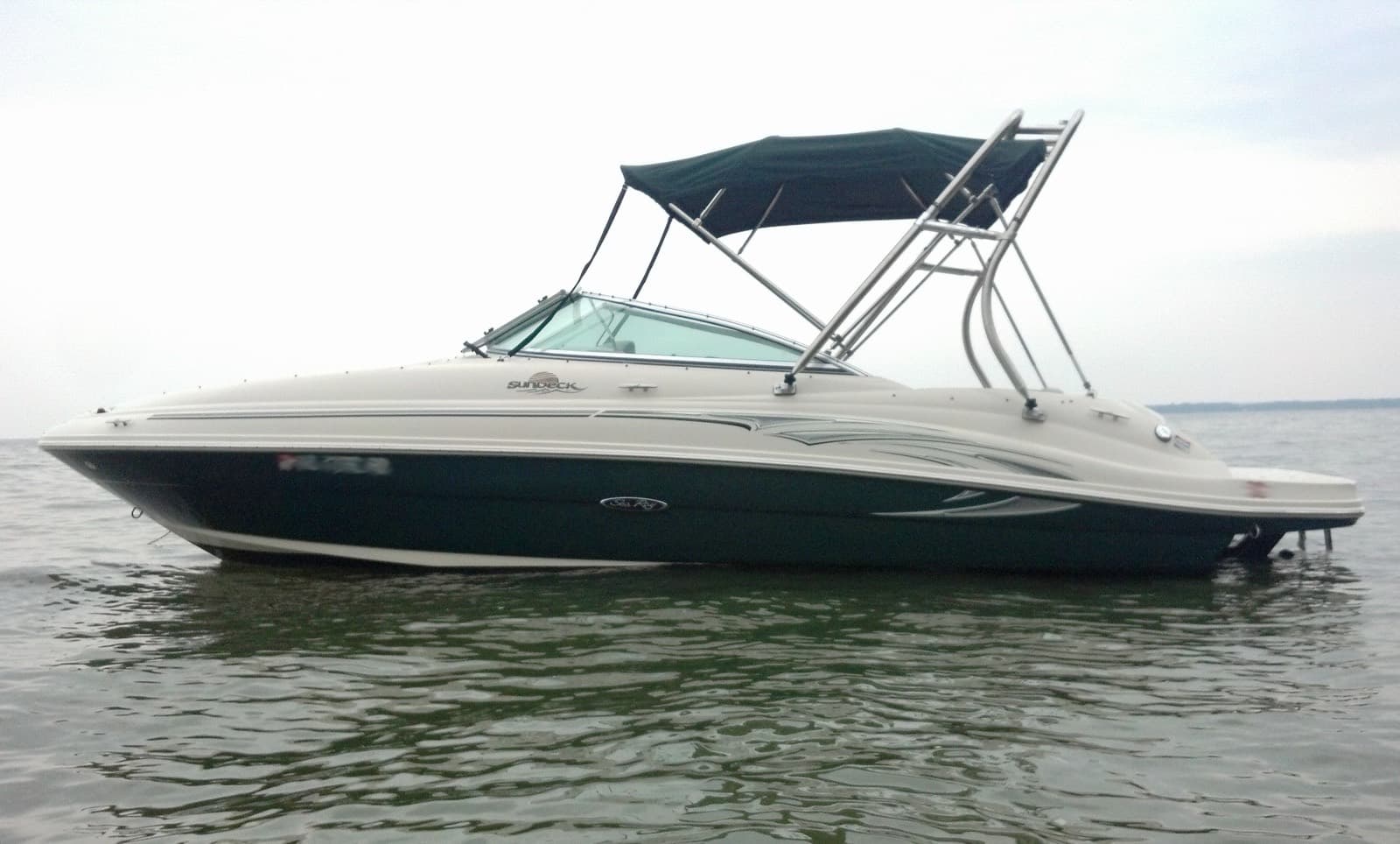 A white and navy bowrider with a bimini top on a wakeboard tower, at anchor on calm water