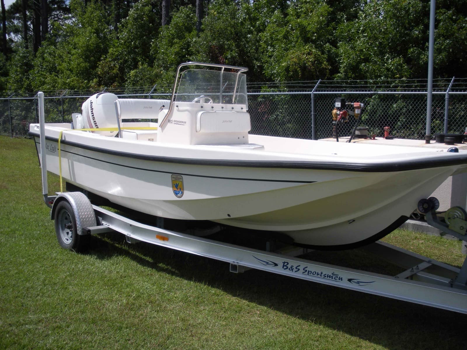 A white center console fishing boat on a trailer, parked on grass