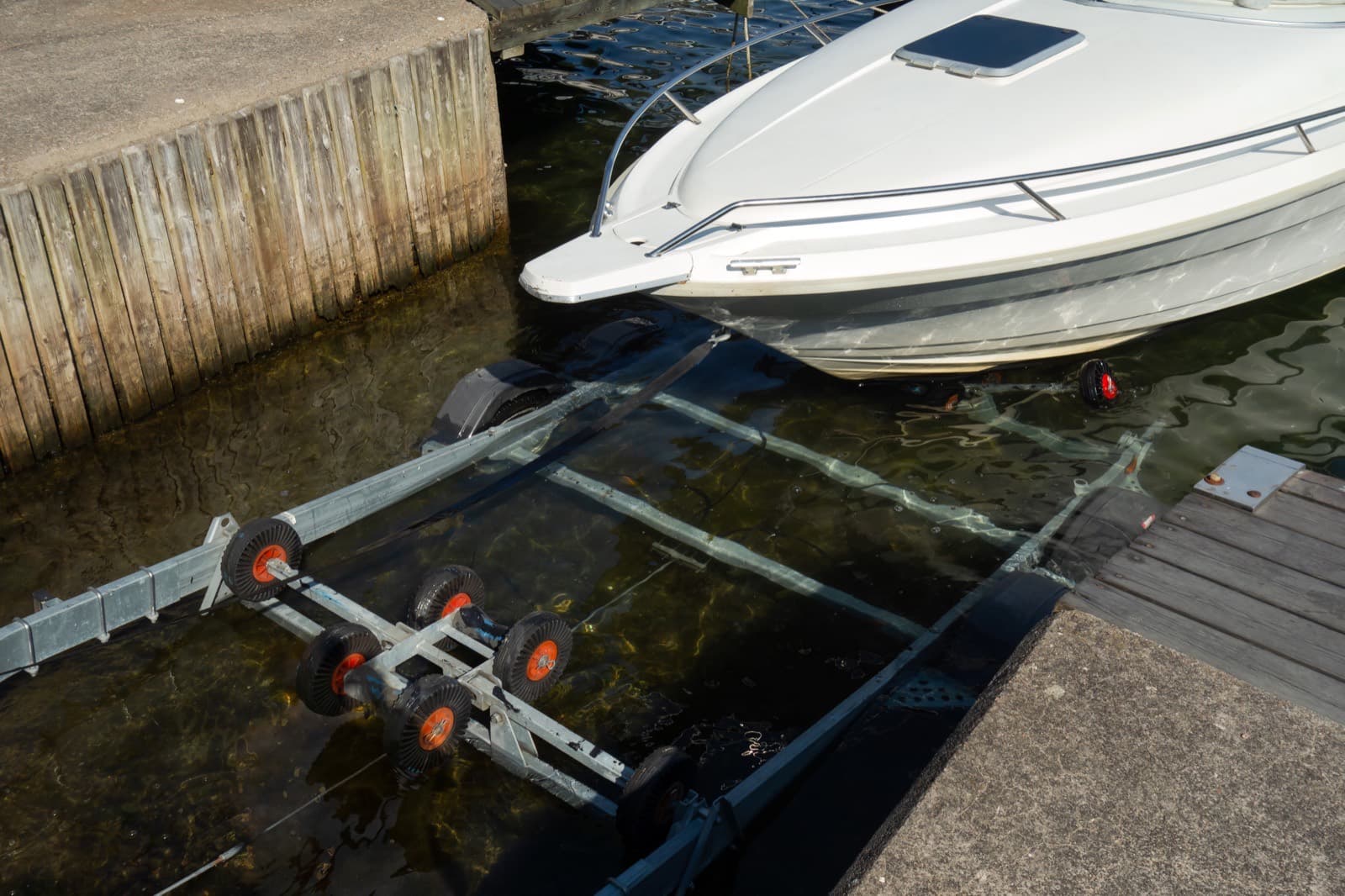 A white boat being winched onto a submerged trailer at a boat ramp