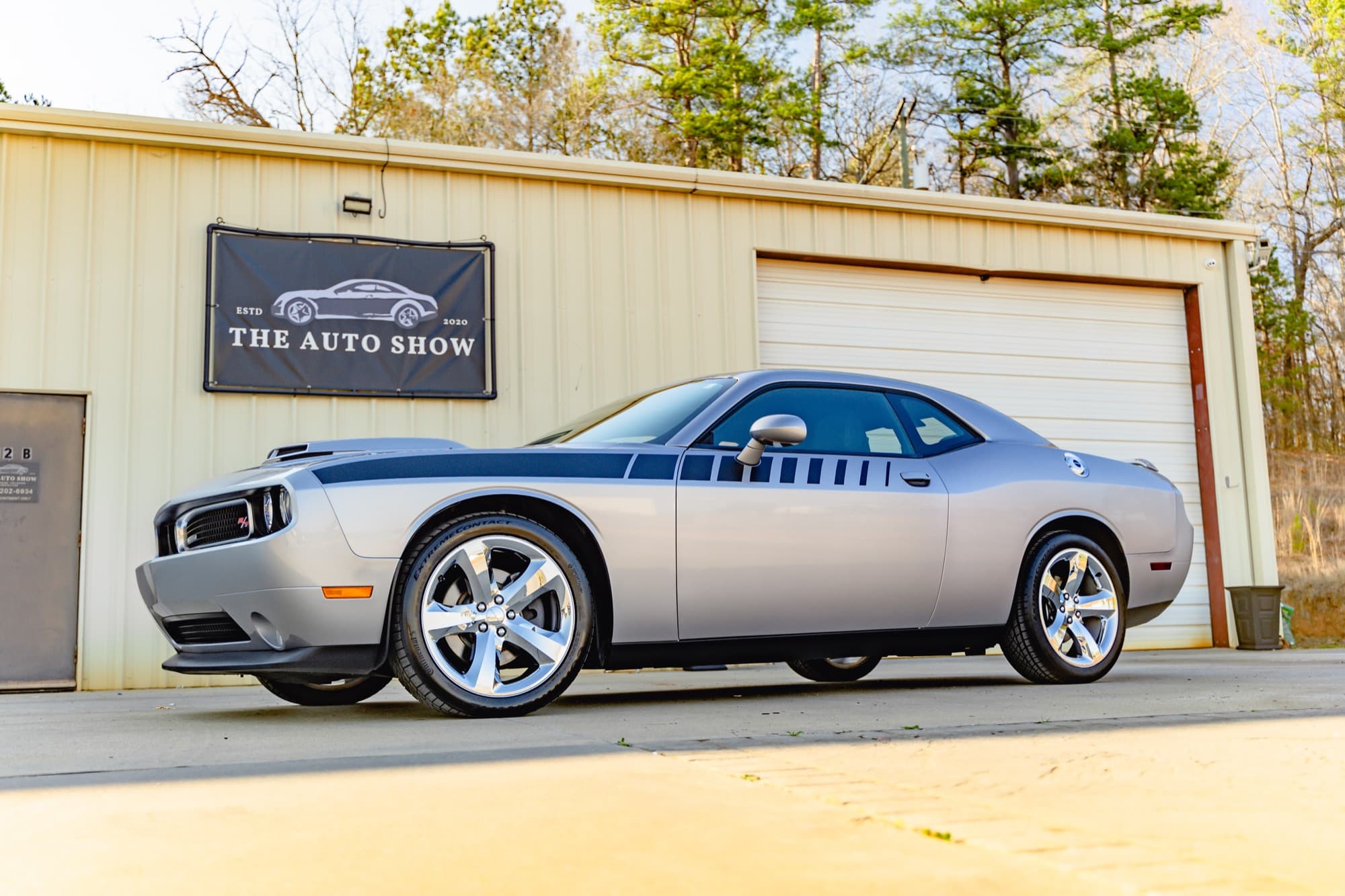 A silver Dodge Challenger with black stripes parked outside The Auto Show