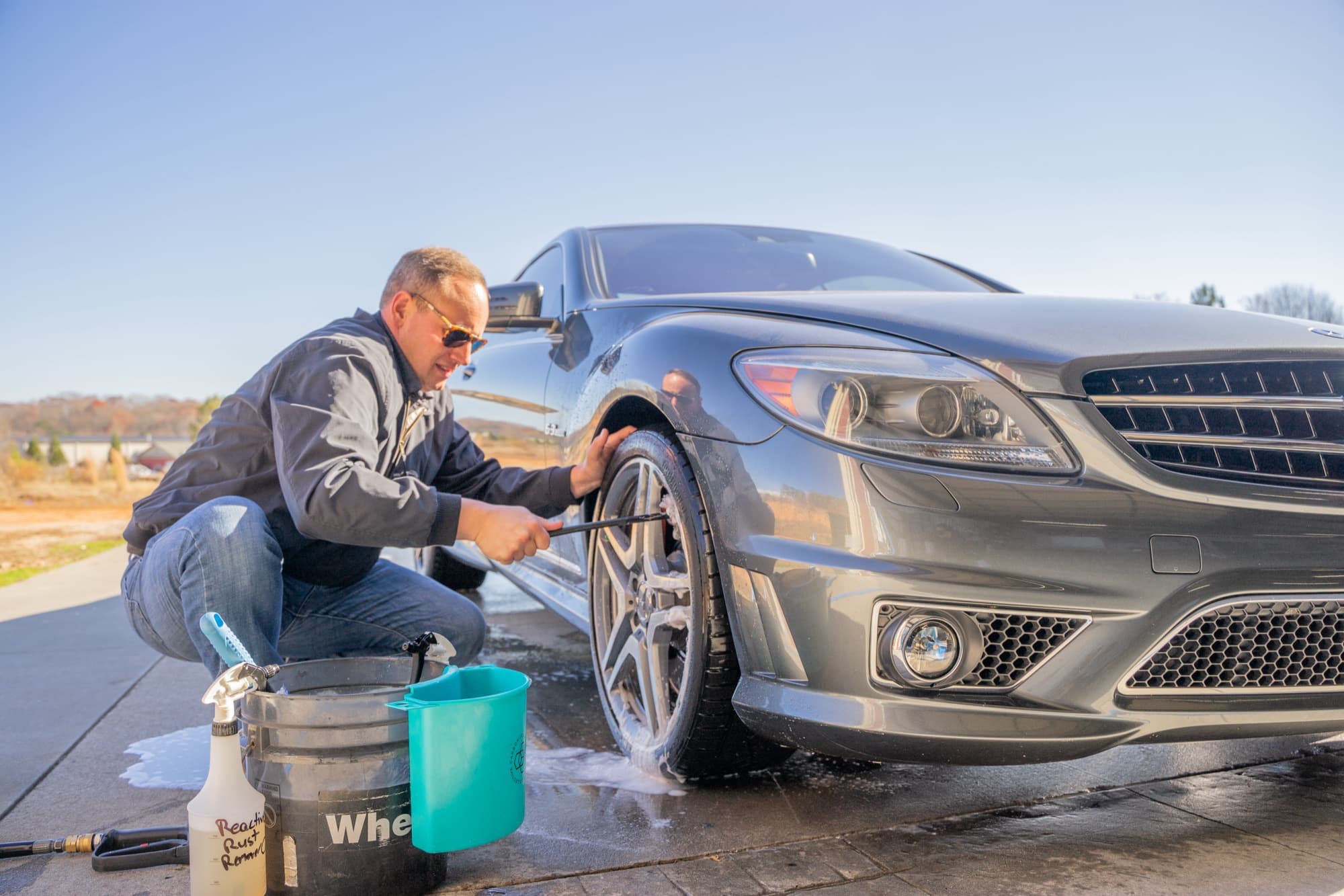 Detailer hand-washing the wheel of a gray Mercedes coupe outside the shop