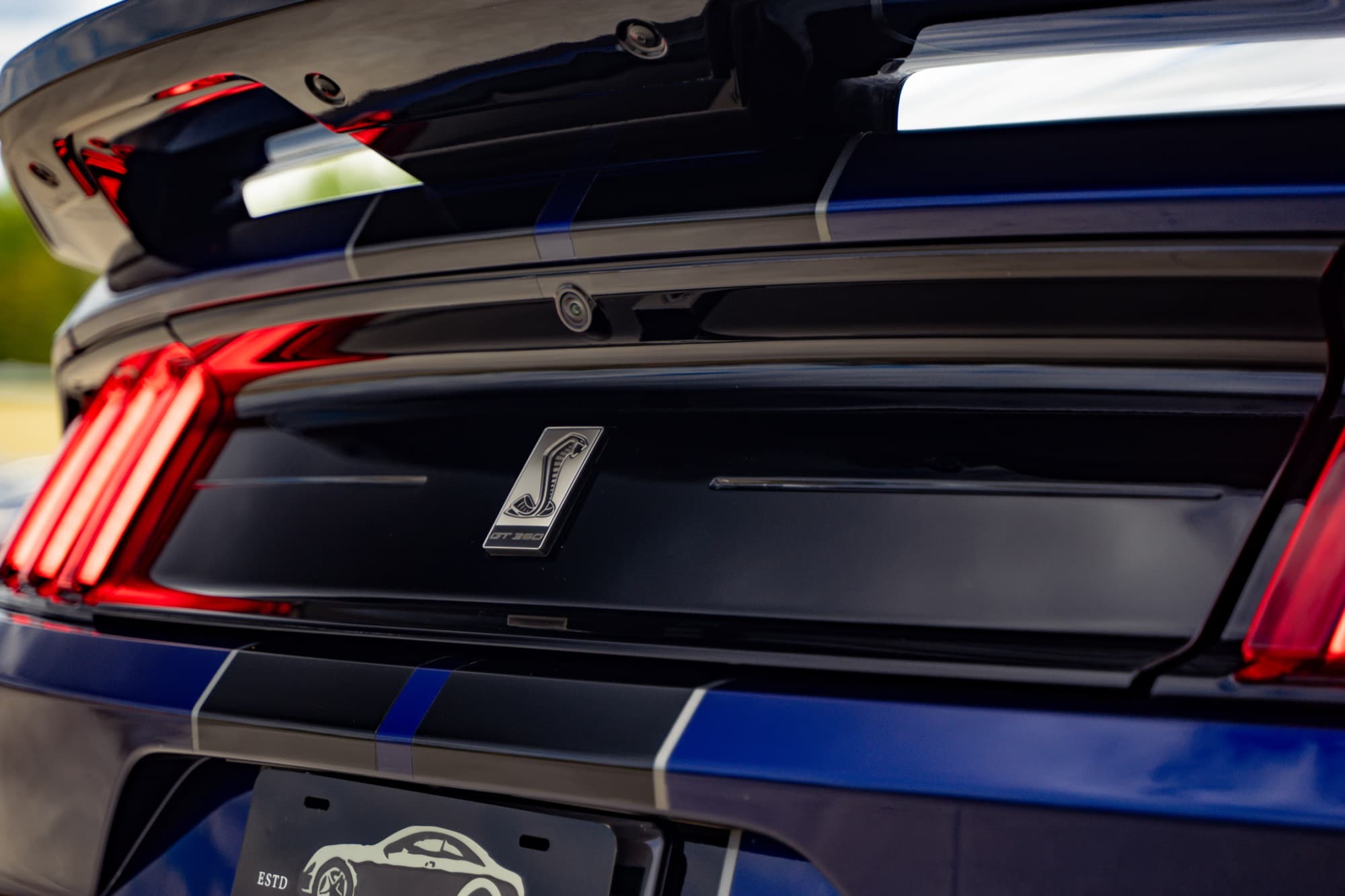 Close-up of the lit red taillights and rear badge of a dark blue Ford Mustang