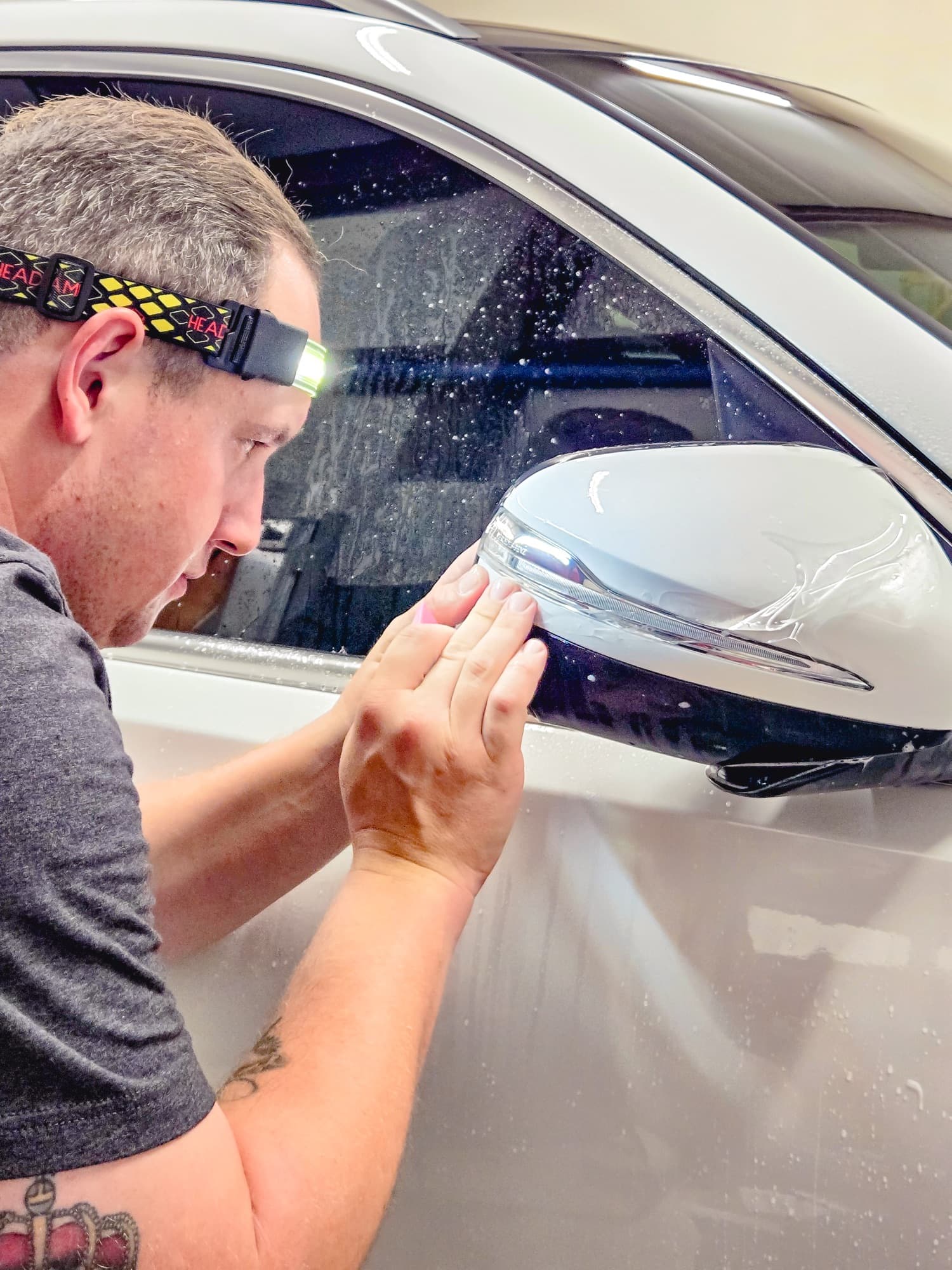 An installer smoothing paint protection film over a white Mercedes mirror