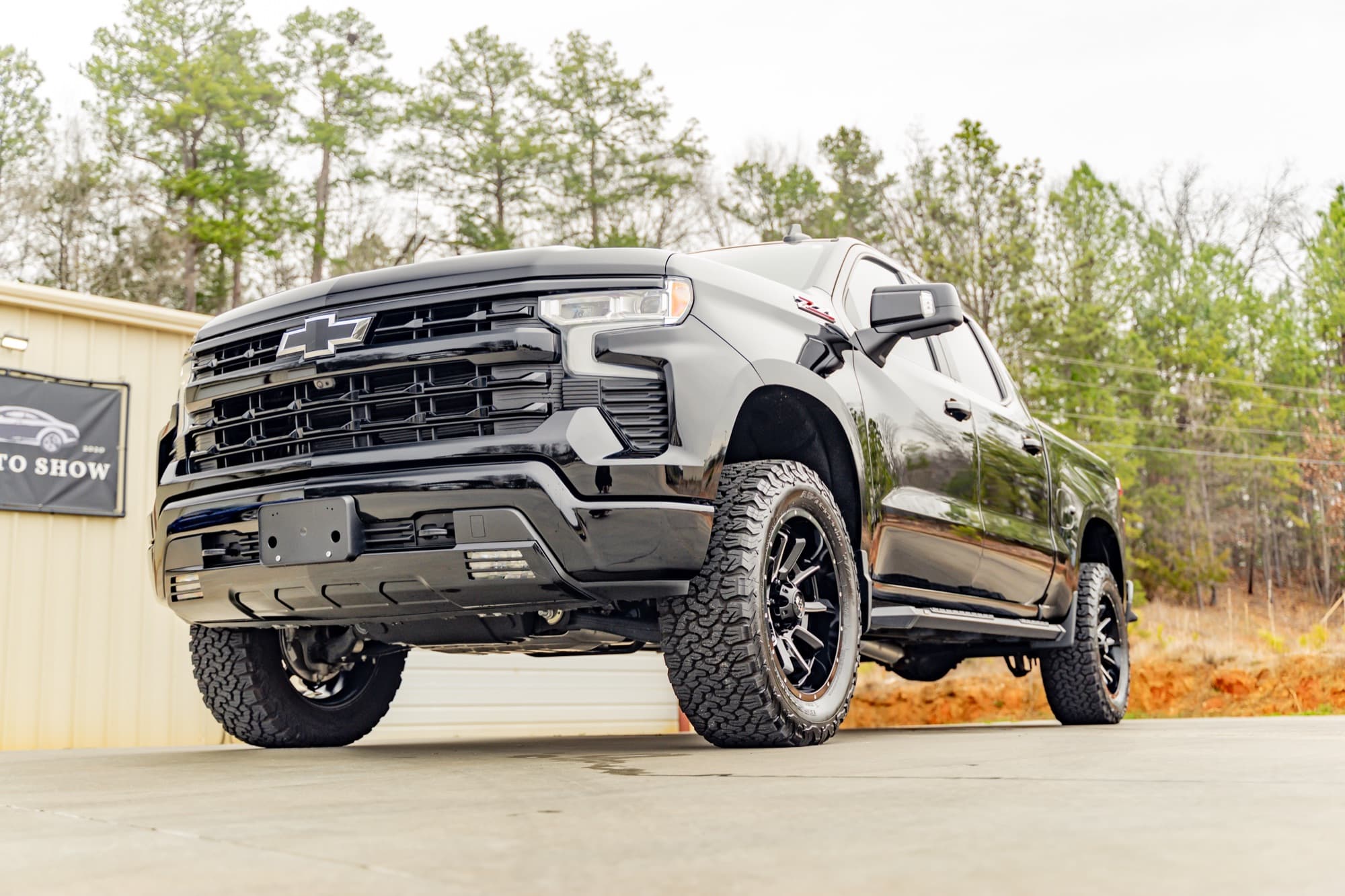 A black Chevrolet Silverado pickup with dark wheels parked outside a shop