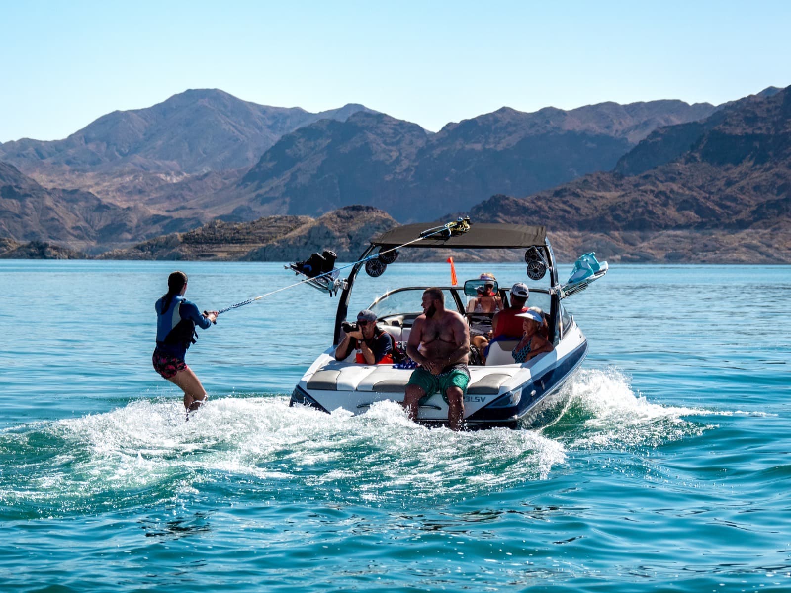 A wake boat with a tower towing a wakeboarder on a mountain lake